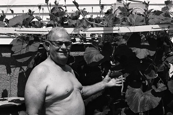 A smiling man standing beside climbing garden plants, in black and white.